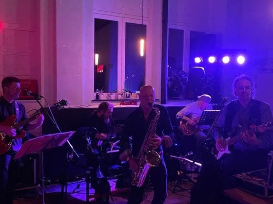 Een band speelt live in de zaal, onder podiumverlichting.