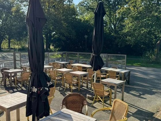 Het terras met rieten stoelen en parasols, tussen de bomen.